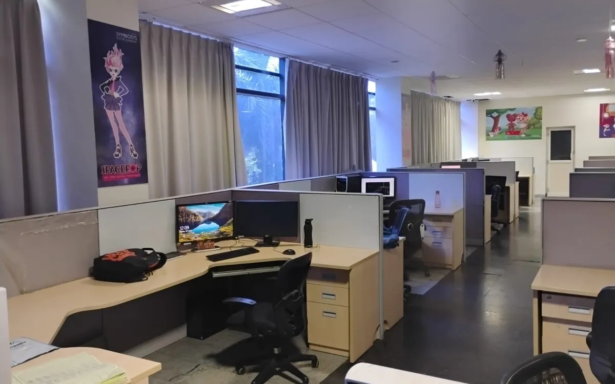 A dual-monitor workstation on the Symbiosys production floor, under a SpacePOP poster