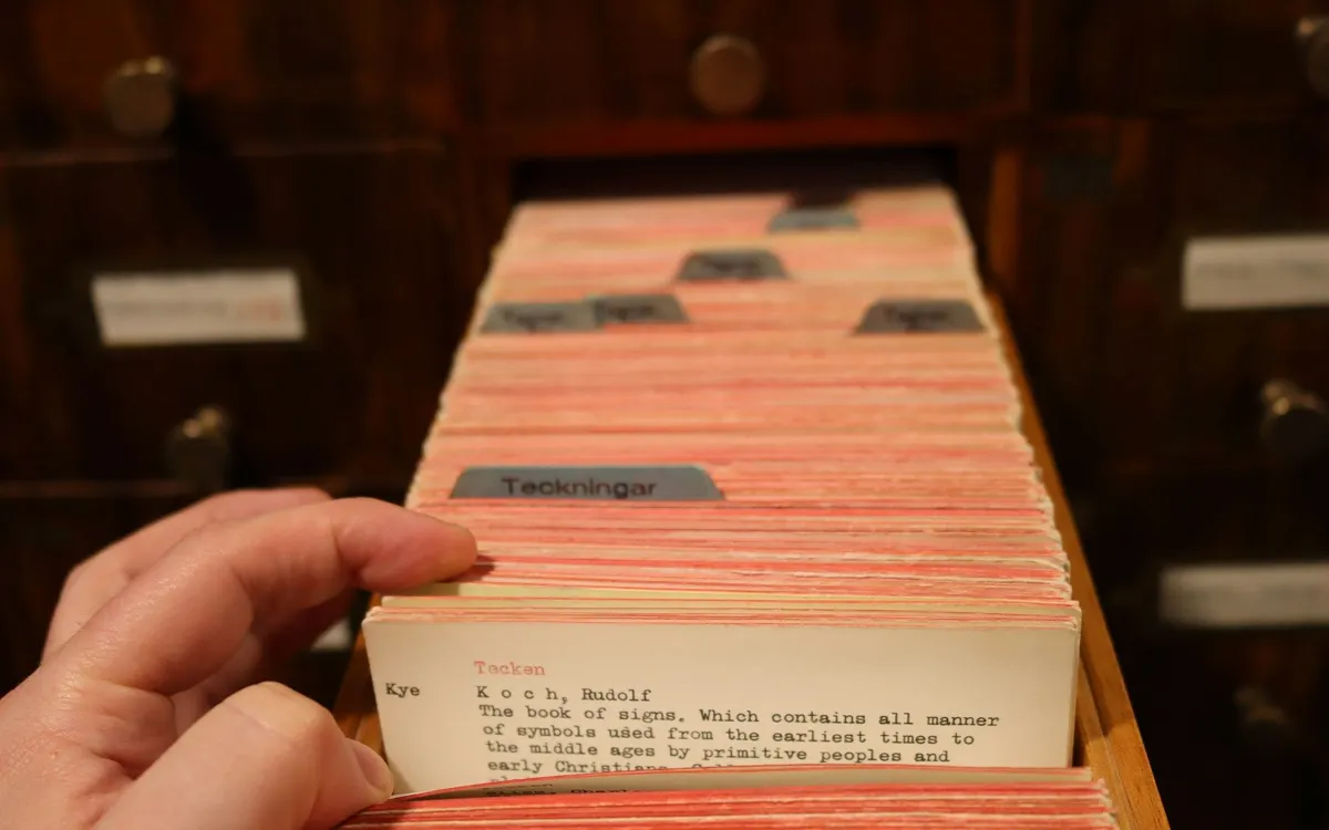 A hand looking through index cards in a library card catalogue