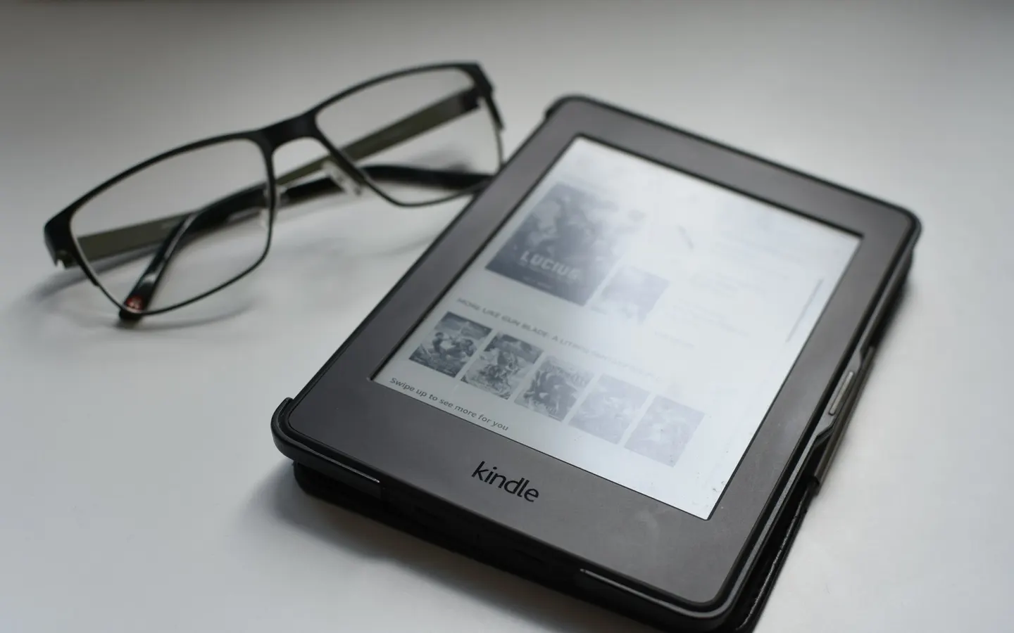 An e-reader showing a digital library, beside a pair of glasses